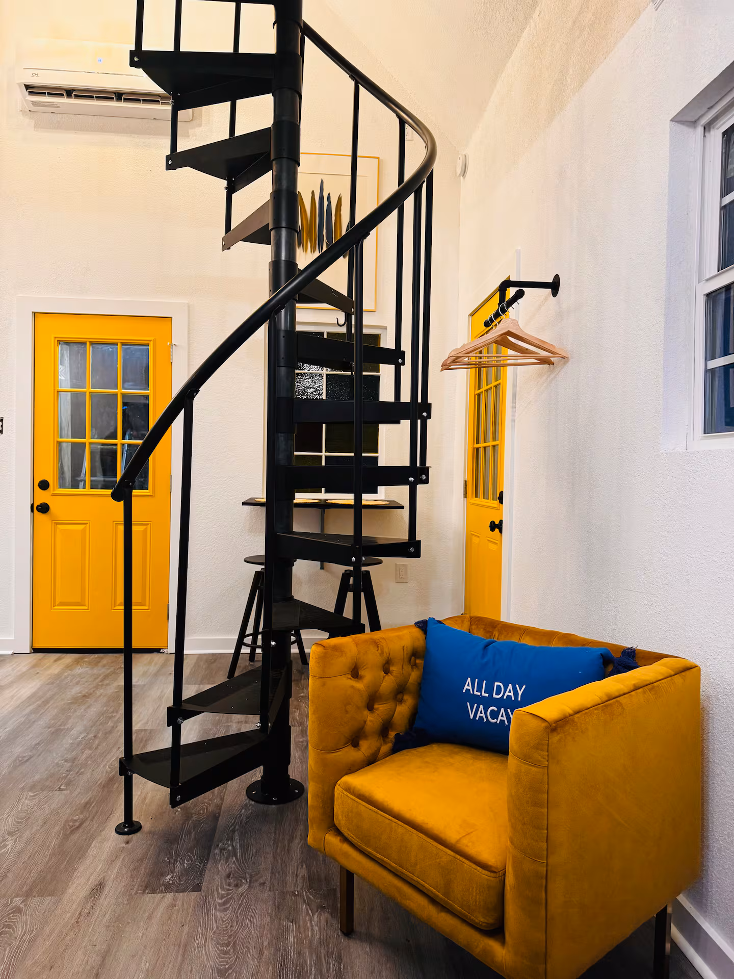 Interior with a black spiral staircase leading to a loft and a mustard velvet chair