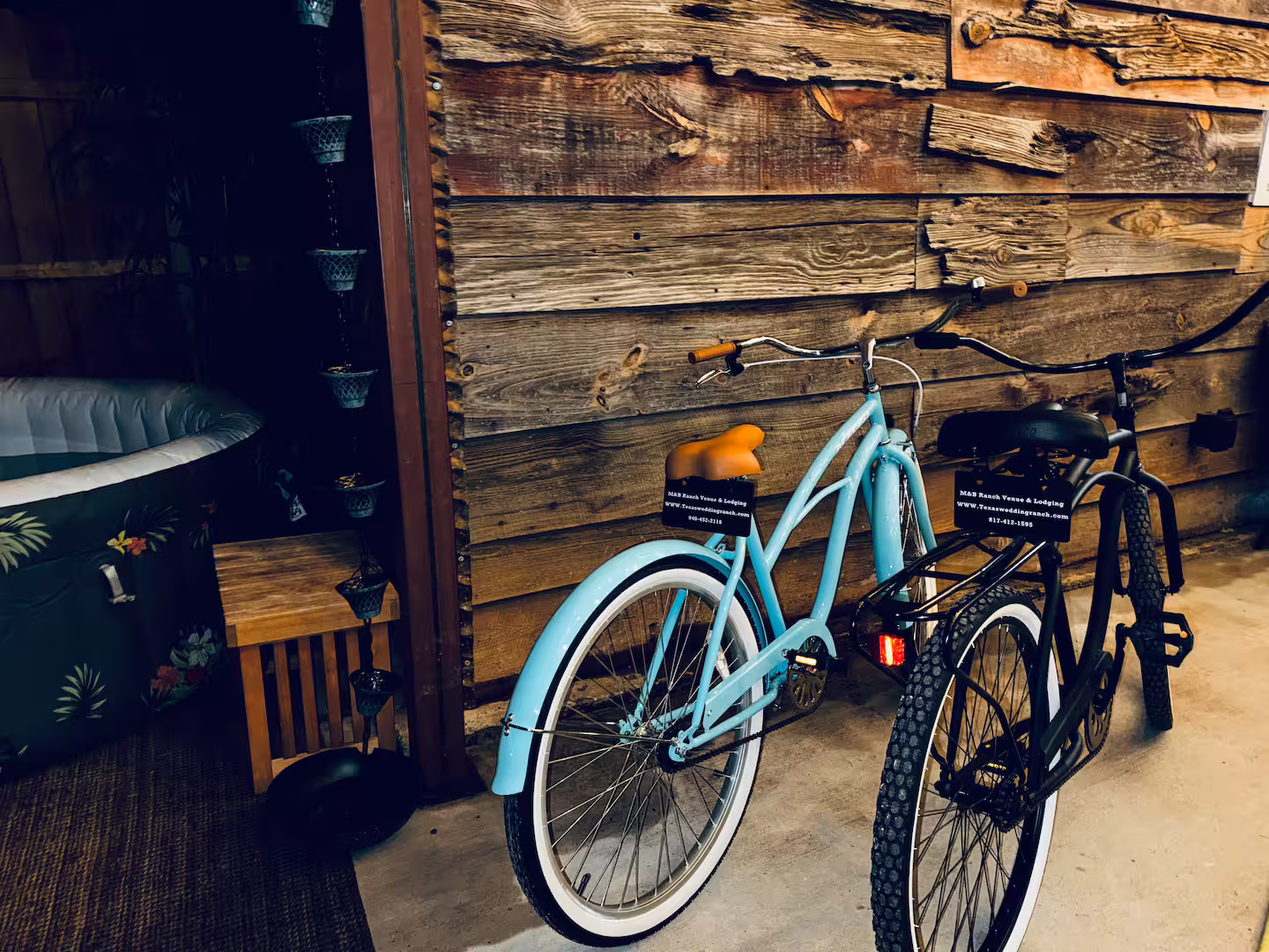 Two M&B Ranch cruiser bikes parked by a reclaimed-wood cabin wall next to a hot tub