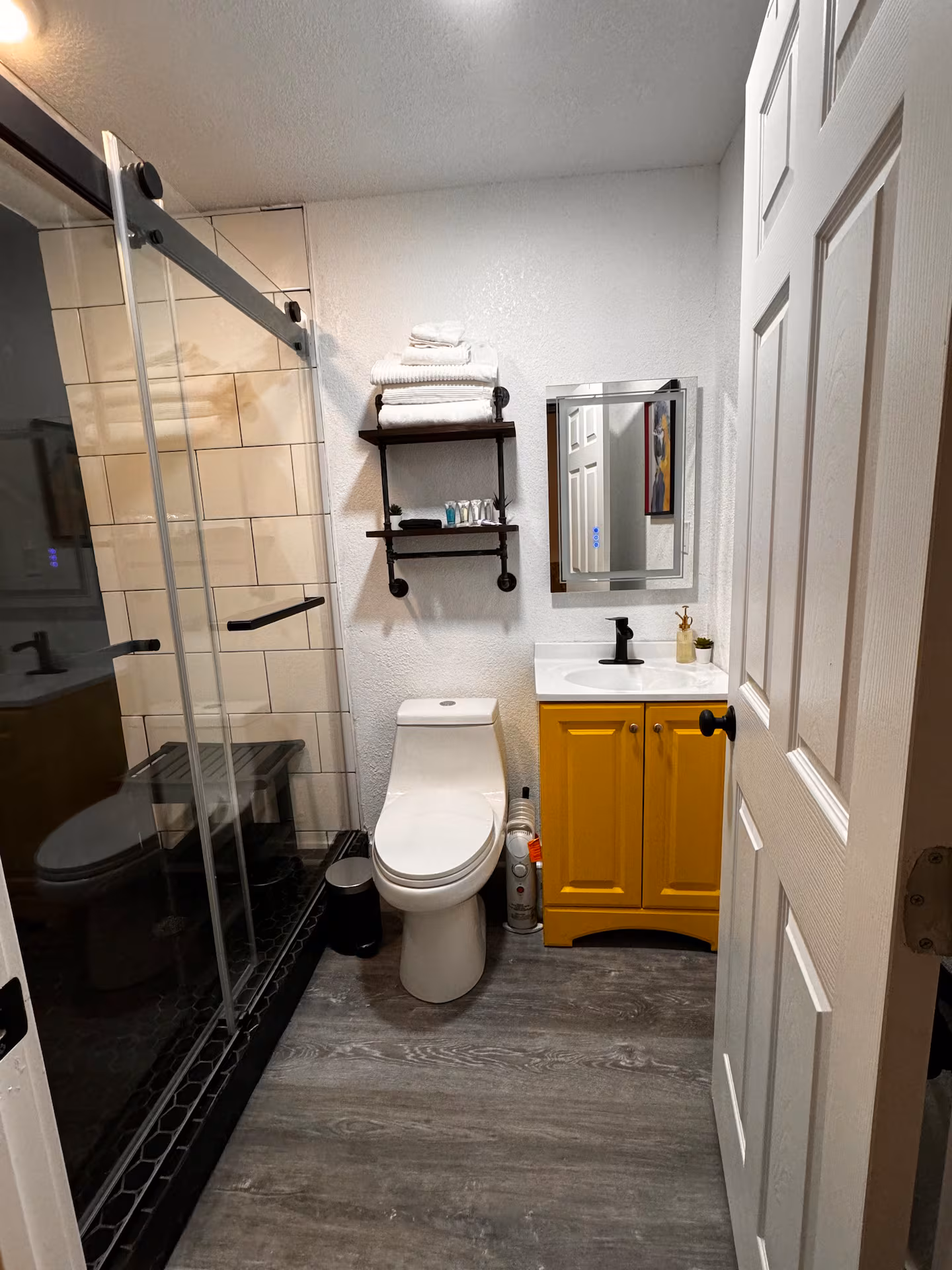 Bathroom with a walk-in tile shower, floating shelves, and a mustard vanity